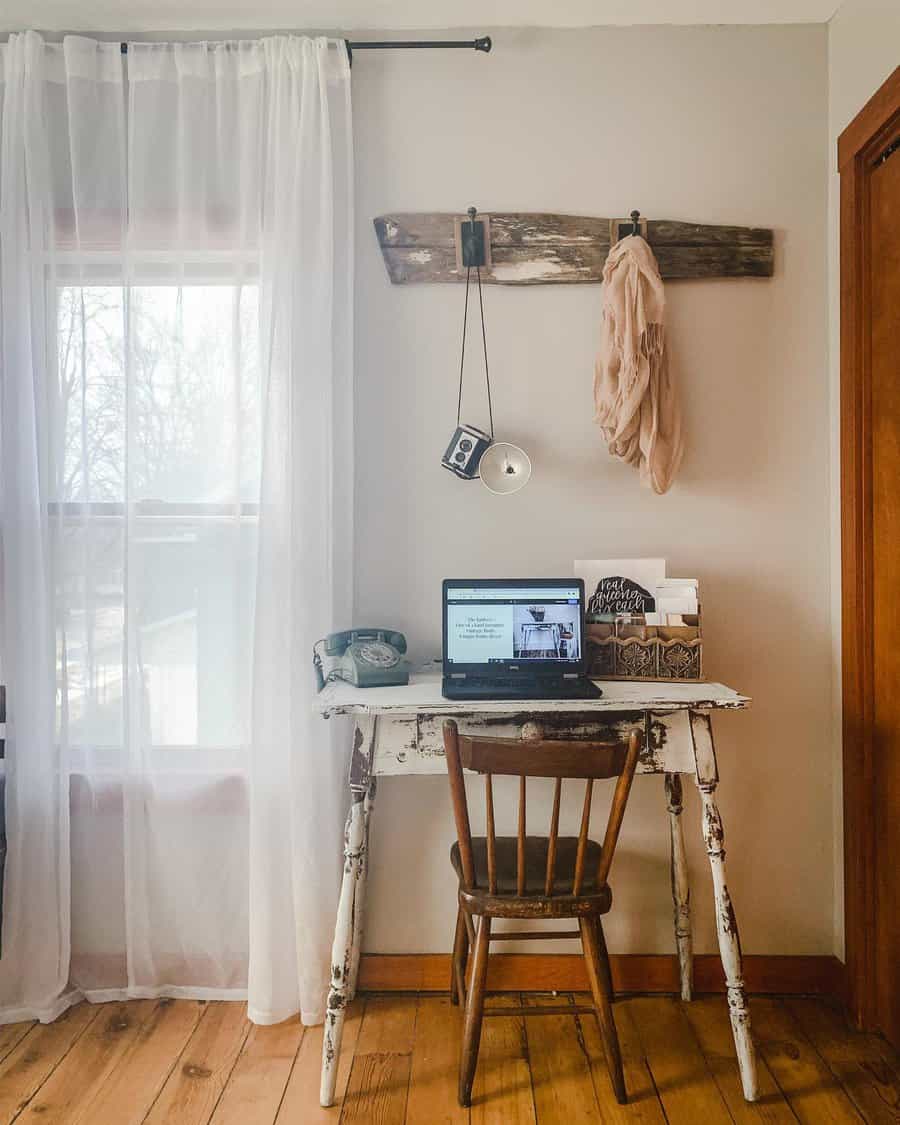 Cozy workspace with a rustic desk, wooden chair, vintage phone, laptop, and decor; sheer curtains cover a sunlit window