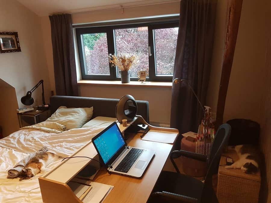 Cozy bedroom office with a wooden desk, laptop setup, and warm lighting, blending work and relaxation in a comfortable space