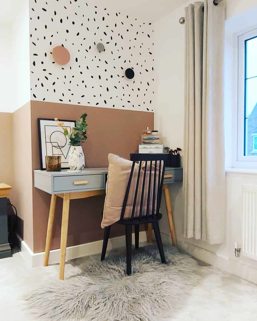 A cozy workspace with a gray desk, black chair, fluffy rug, and artistic decor on the wall near a window with curtains