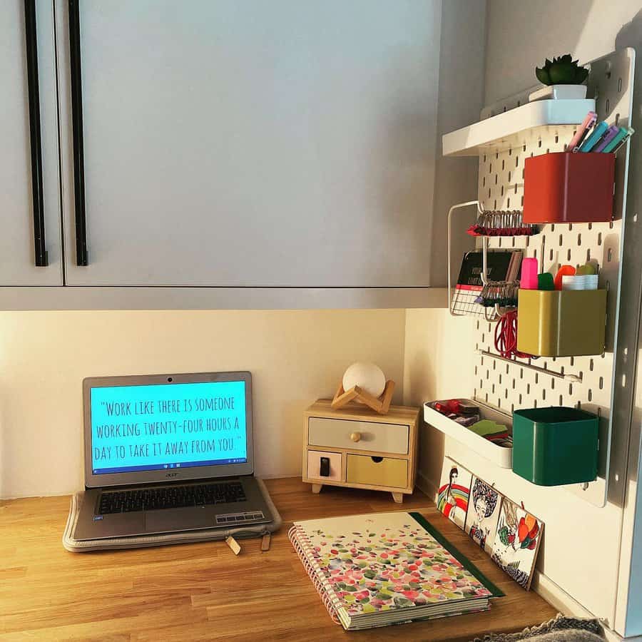 Organized workspace with a laptop, motivational quote on screen, notebooks, and stationery on wooden desk and wall shelves