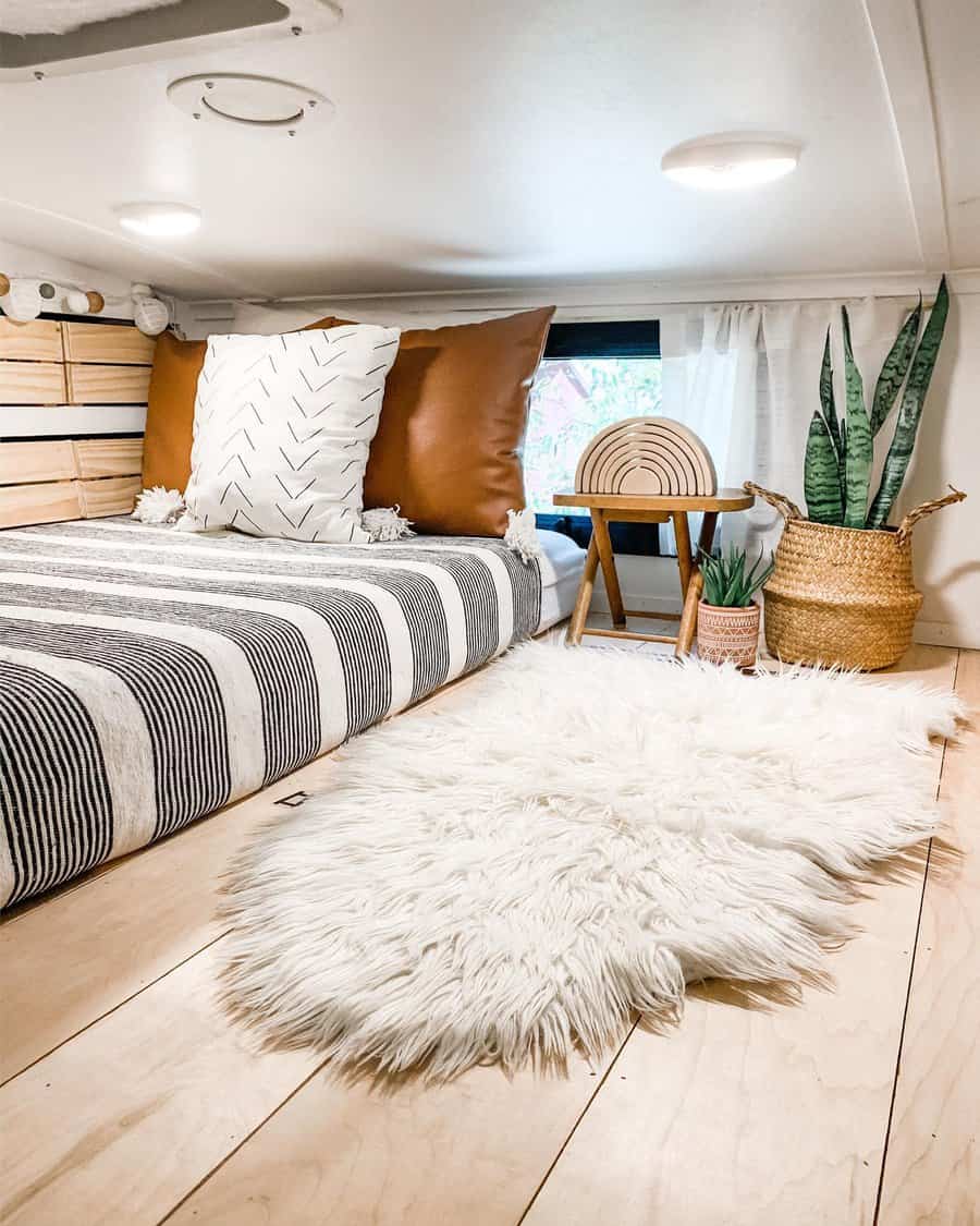 A cozy and minimalist RV bedroom featuring striped bedding, plush pillows, a small table, and indoor plants for a relaxed vibe.