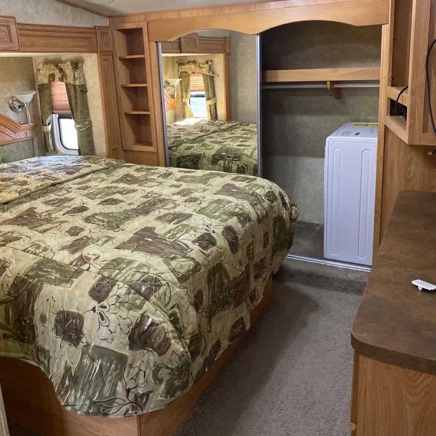 A traditional RV bedroom with wood furniture, a floral bedspread, a mirror wardrobe, and a compact laundry area.