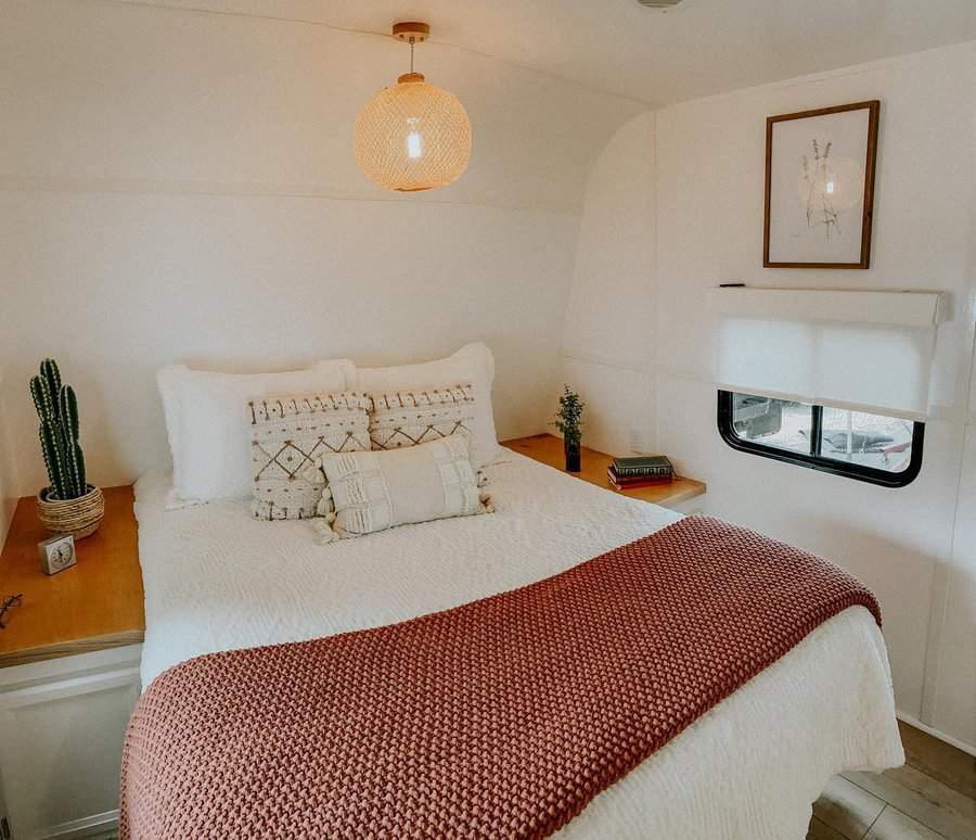 A serene and minimalist RV bedroom with cozy textiles, soft lighting, a small cactus, and a framed botanical print, creating a warm and inviting space.