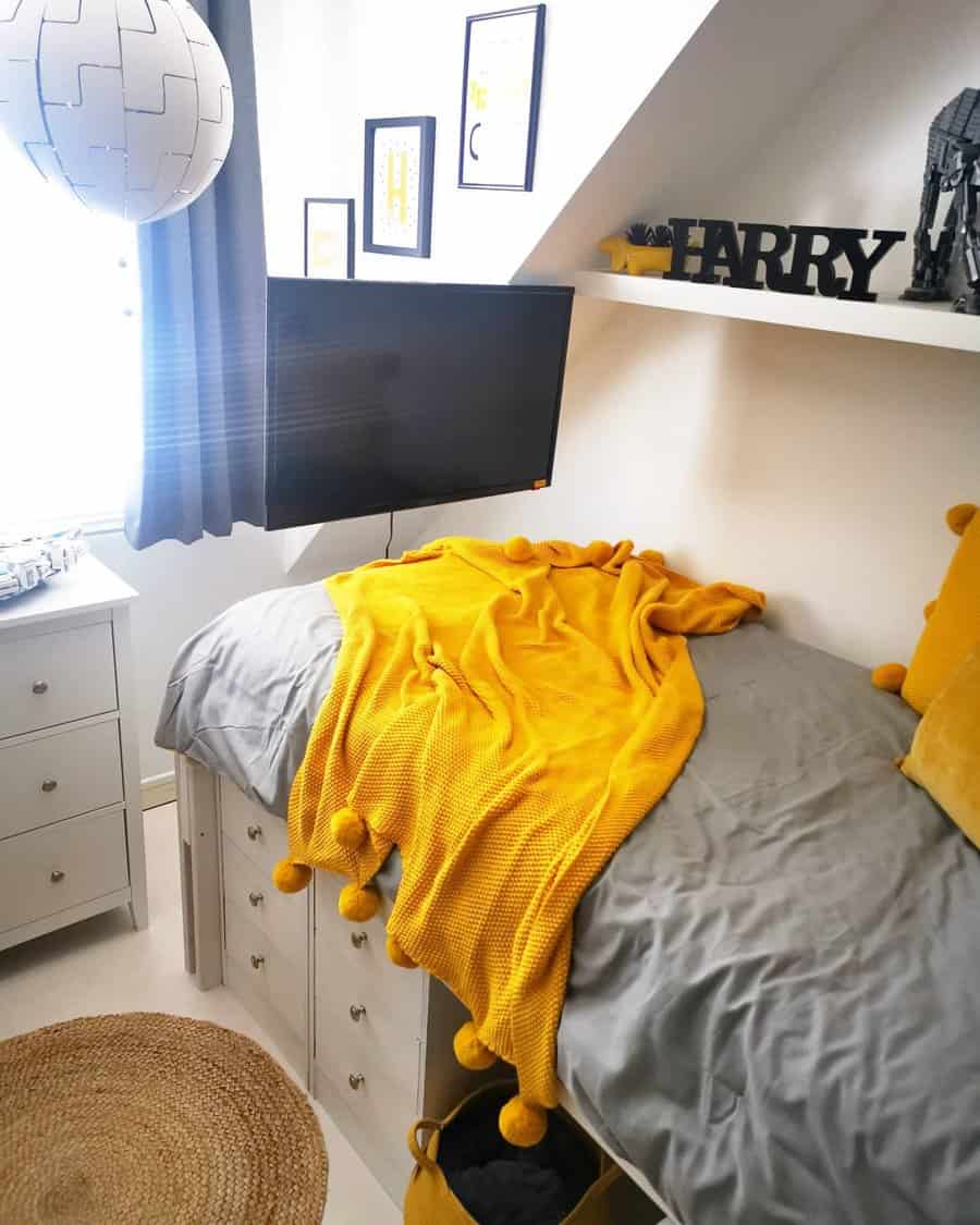 A compact bedroom with a raised bed featuring built-in drawer storage, a floating shelf, and a cozy yellow and gray color scheme for a stylish look