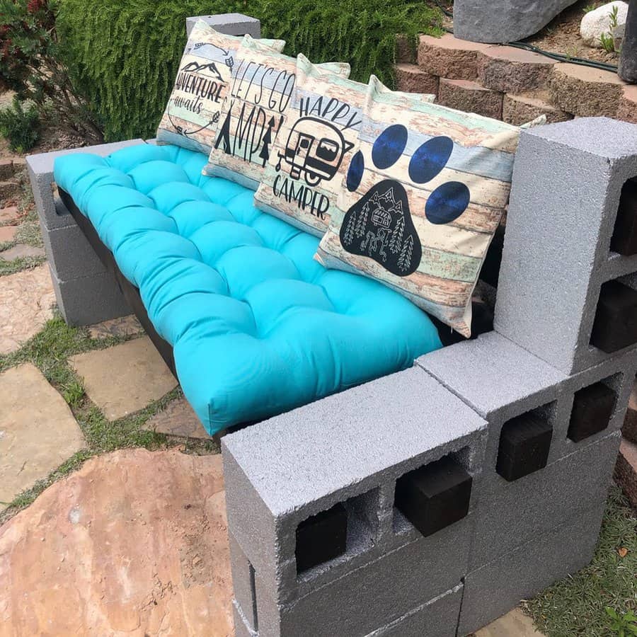 DIY cinder block bench with a bright blue cushion and rustic camping-themed pillows, creating a cozy and stylish outdoor seating area