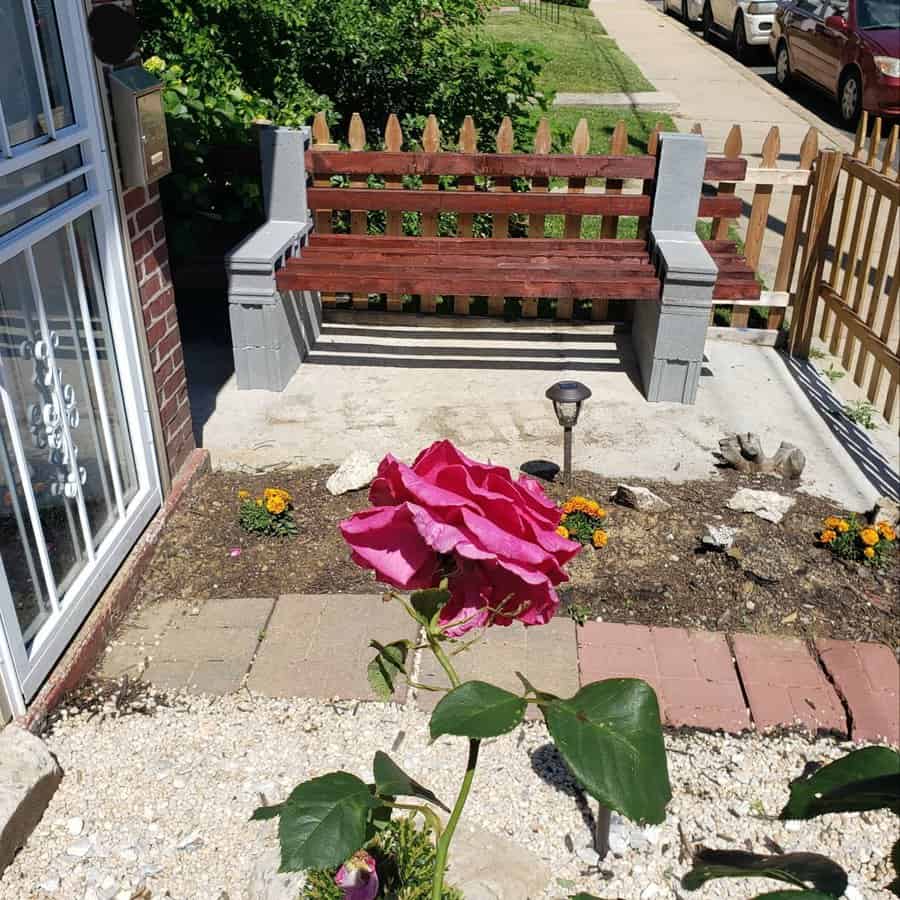 DIY cinder block and wood bench in a front yard, framed by a picket fence and a blooming pink rose, creating a charming outdoor seating area