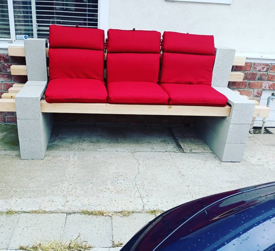 DIY cinder block bench with natural wood beams and bold red cushions, creating a stylish and comfortable outdoor seating area against a brick wall