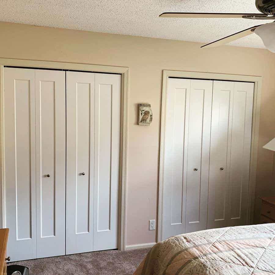 Bedroom with two white closets, a ceiling fan, beige walls, and a bed partially visible in the foreground