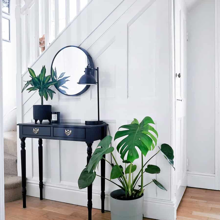 Stylish black console table with gold handles in a bright entryway, paired with a round mirror, greenery, and a sleek black lamp.