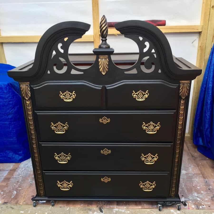 Elegant black-painted dresser with ornate gold handles and intricate carved detailing, featuring a decorative arch and finial accent.