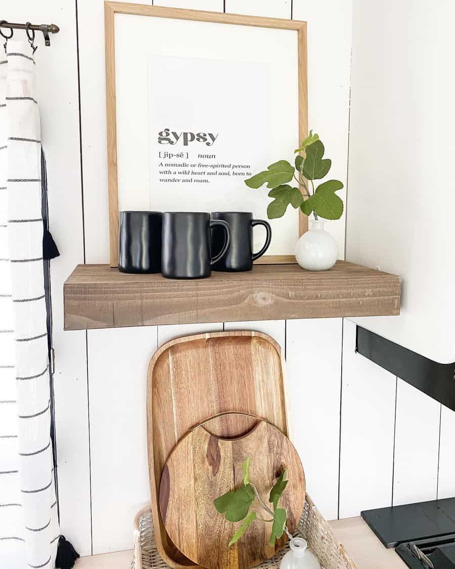 A stylish black-and-white RV corner featuring a framed "gypsy" print, black mugs, a small plant, and wooden trays for a minimalistic, cozy touch.