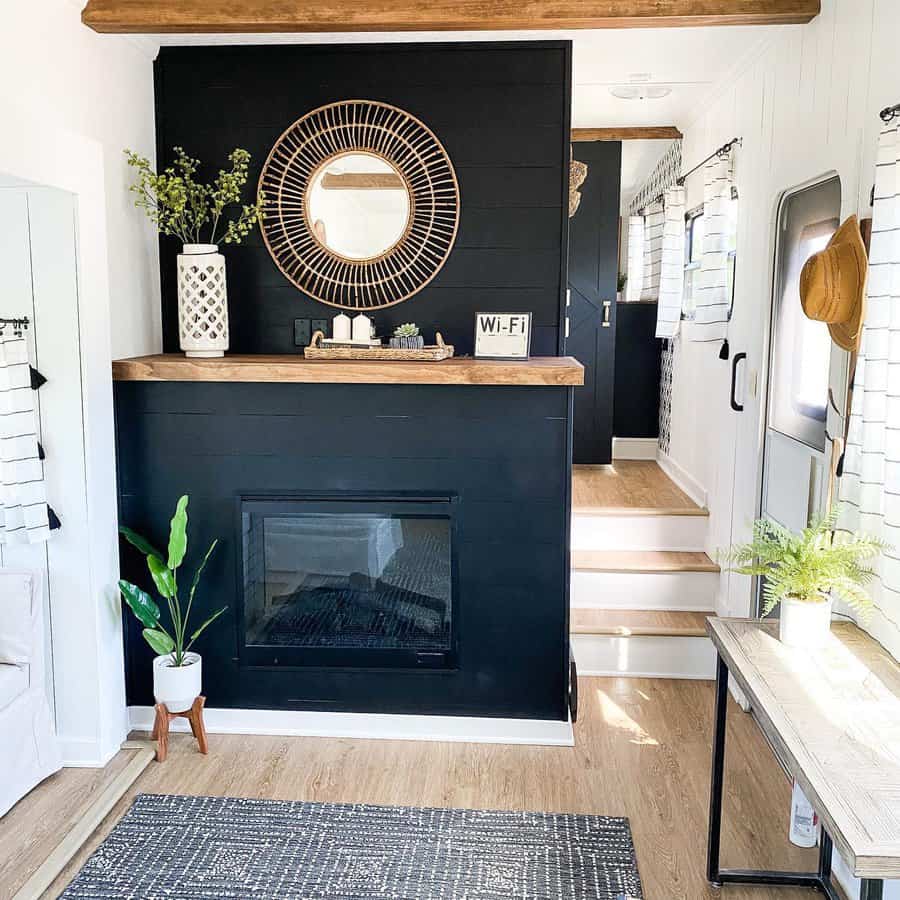 A stylish RV living area featuring a black feature wall with a fireplace, a round mirror, plants, and a warm, welcoming space with wooden accents.