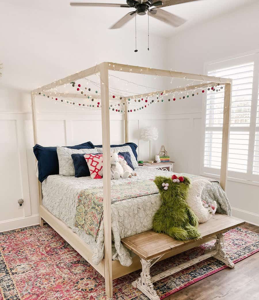 Cozy bedroom with a canopy bed decorated with string lights and pom-poms, colorful pillows, and a green pillow resembling a monster