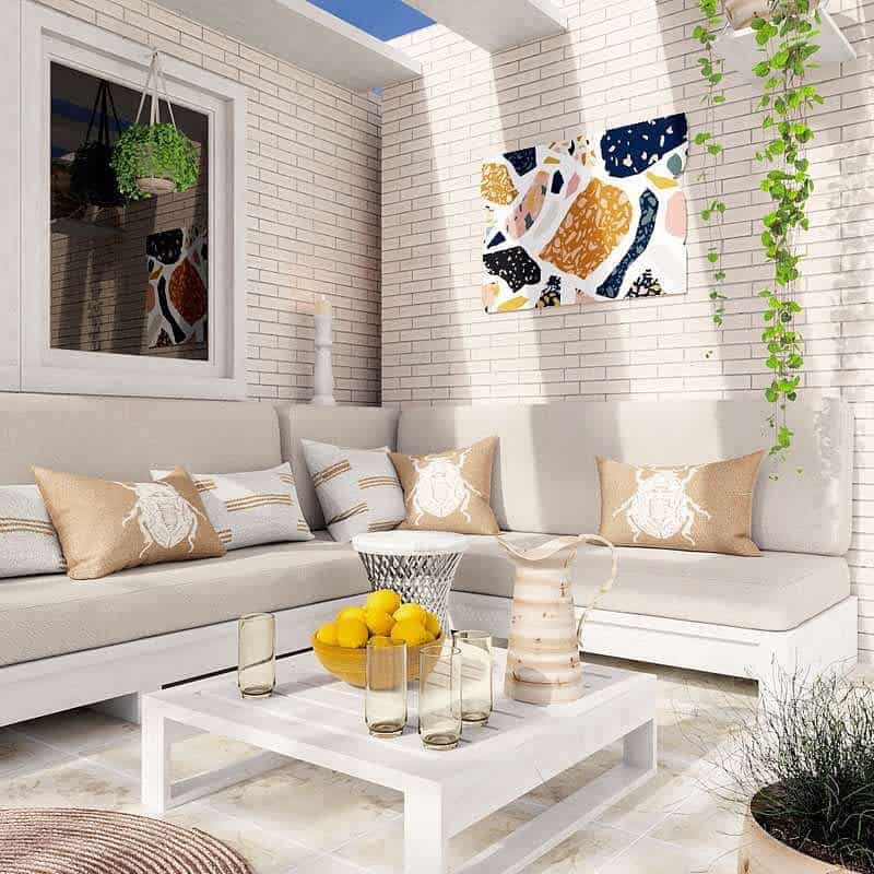 Outdoor patio with white L-shaped sofa, beige cushions, abstract wall art, and a white coffee table with a fruit bowl and drinks