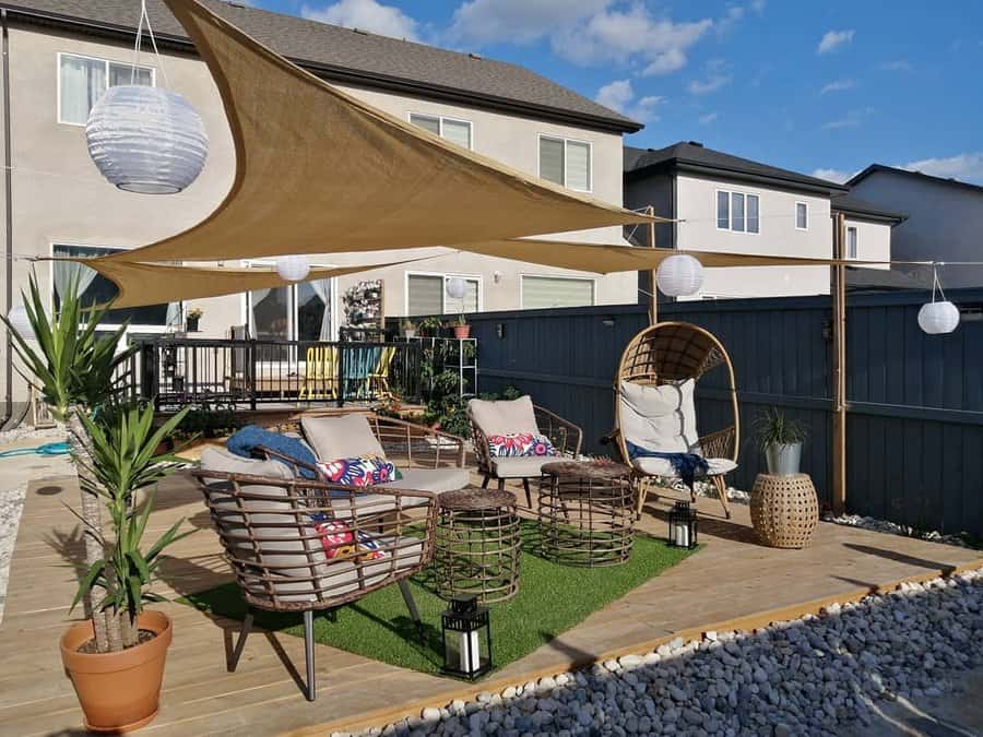 Outdoor patio with wicker chairs, a hanging chair, and a shade sail; decor includes potted plants, lanterns, and paper lanterns