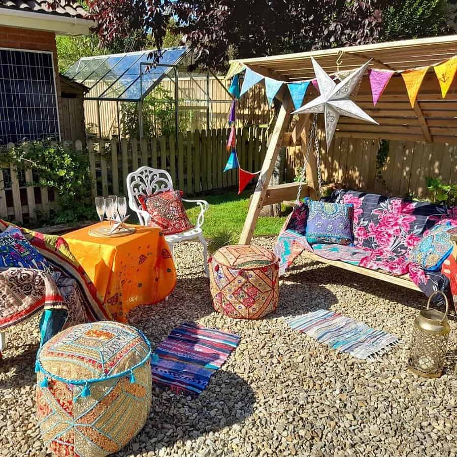 Colorful bohemian garden setup with cushions, poufs, a table, bunting, and a star hanging on a wooden frame, surrounded by plants