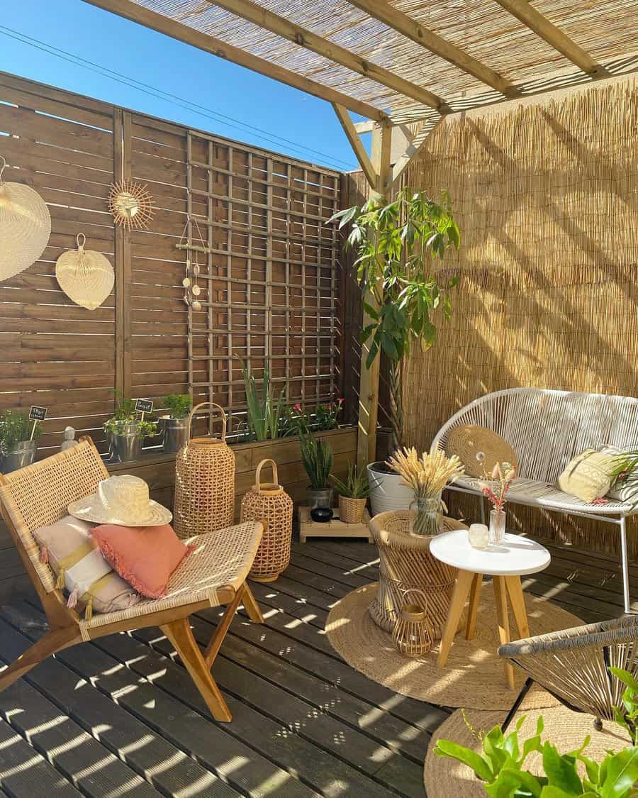 Cozy outdoor patio with wicker chairs, potted plants, and decorative baskets. Wooden privacy screen and natural light create a serene vibe