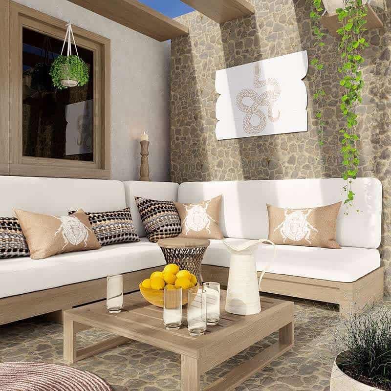 Stylish outdoor patio with white sofas, patterned pillows, wooden table, and decor featuring a small tree, lemons, and glassware for added details