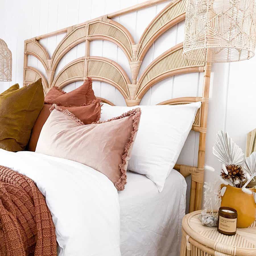 Cozy bed with layered pillows in pink, brown, and white, featuring a rattan headboard and matching side table with decor items