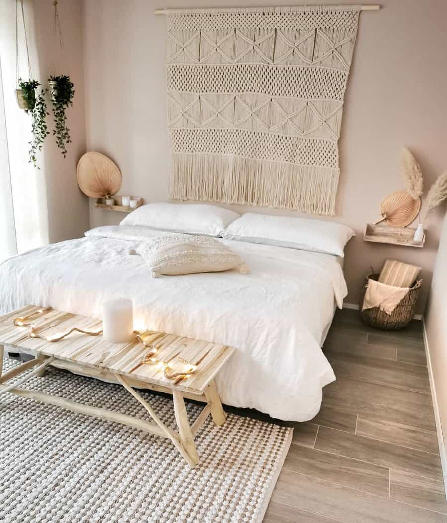 Boho-style bedroom with a white bed, macramé wall hanging, wooden bench, woven rug, and plants