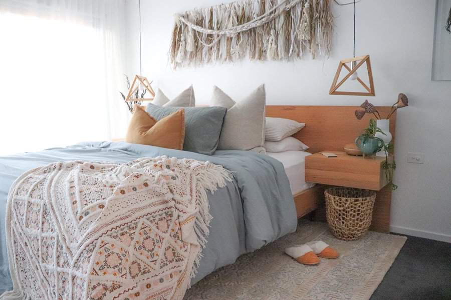 Cozy bedroom with a wooden headboard, blue and white bedding, pillows, a decorative blanket, hanging lights, and wall-hanging decor above