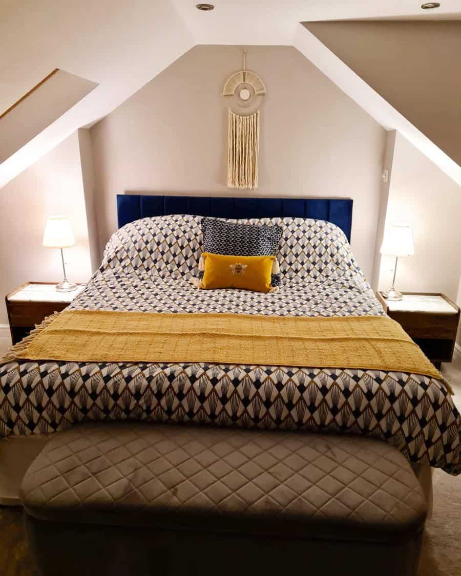 Boho attic bedroom with a navy headboard, geometric bedding, and warm mustard accents. Cozy lighting and macramé decor add a stylish touch.