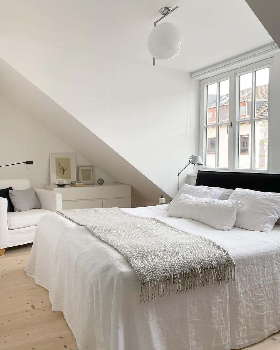 Minimalist attic bedroom with a black headboard, white linens, and soft natural light. Clean lines and cozy textures create a serene retreat.