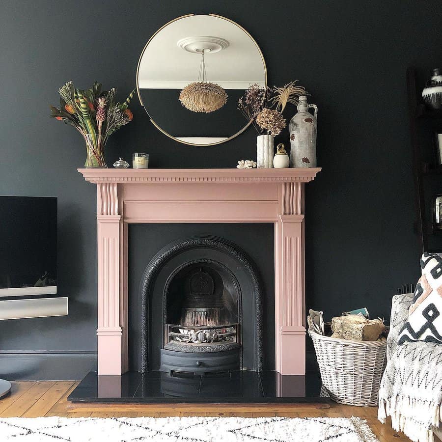 Chic living room with pink fireplace, round mirror, dark walls, and rustic decor including a wicker basket and dried plants