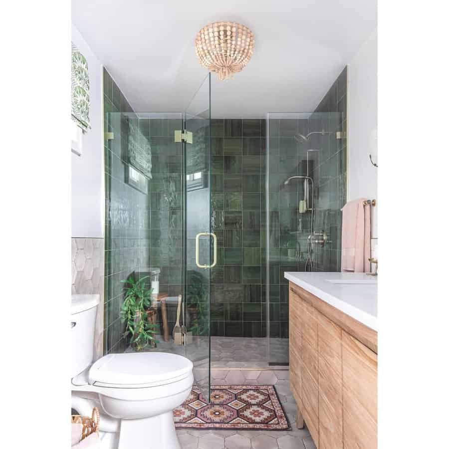 Green tiled bathroom with wooden cabinets and a glass shower door