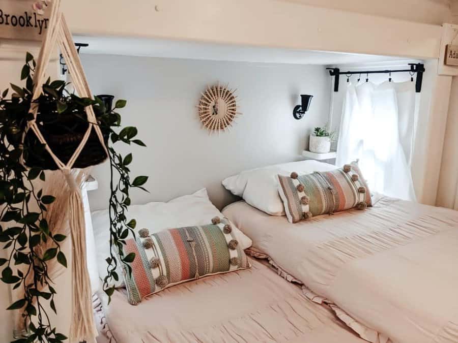 A cozy boho RV bedroom with twin beds, colorful pom-pom pillows, a hanging plant, and a round mirror for a warm, inviting atmosphere.