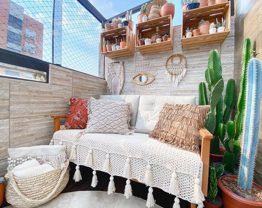 Boho-chic small balcony with a cozy cushioned bench, macrame decor, cacti, hanging wooden shelves with potted plants, and textured pillows