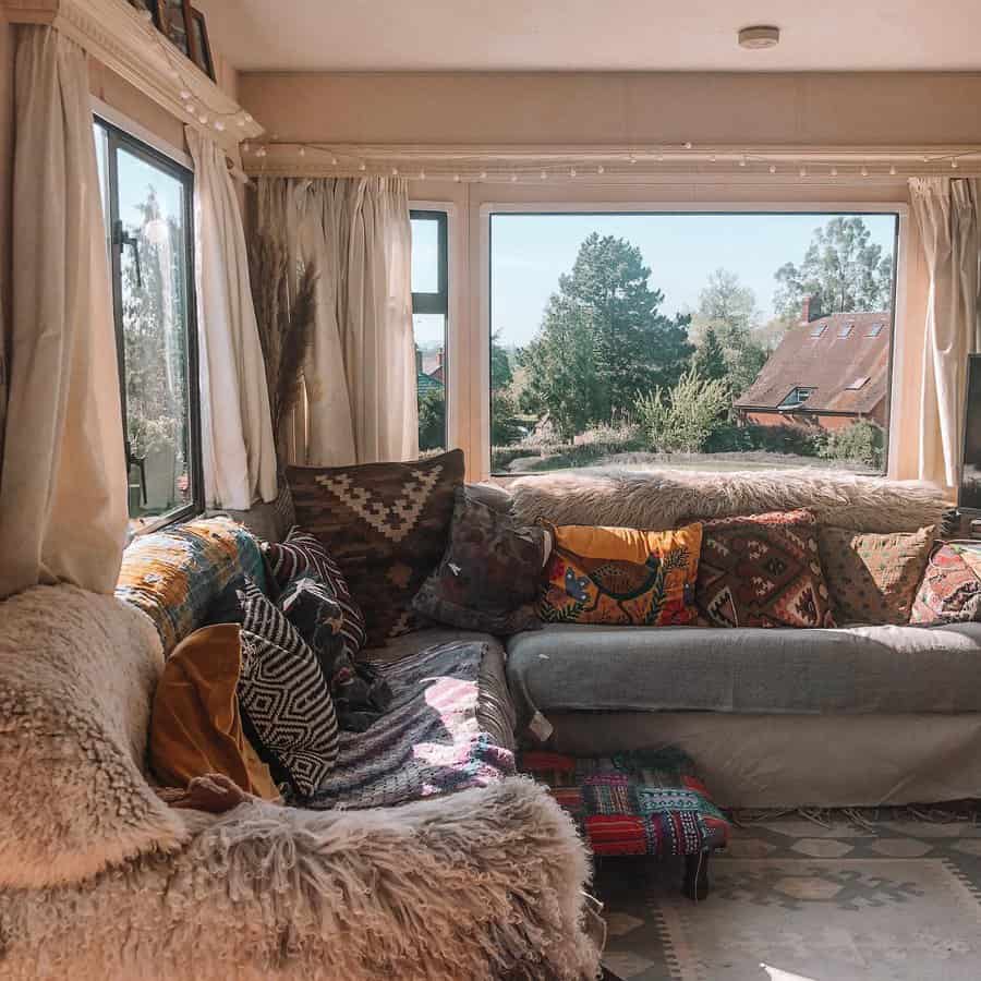 Boho living room with a sheepskin-covered sectional, colorful patterned pillows, and large windows offering a serene countryside view