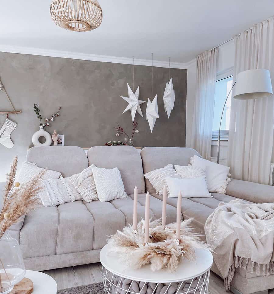 Minimalist boho living room with a neutral-toned sectional, textured pillows, soft drapes, hanging star decor, and a cozy candle centerpiece