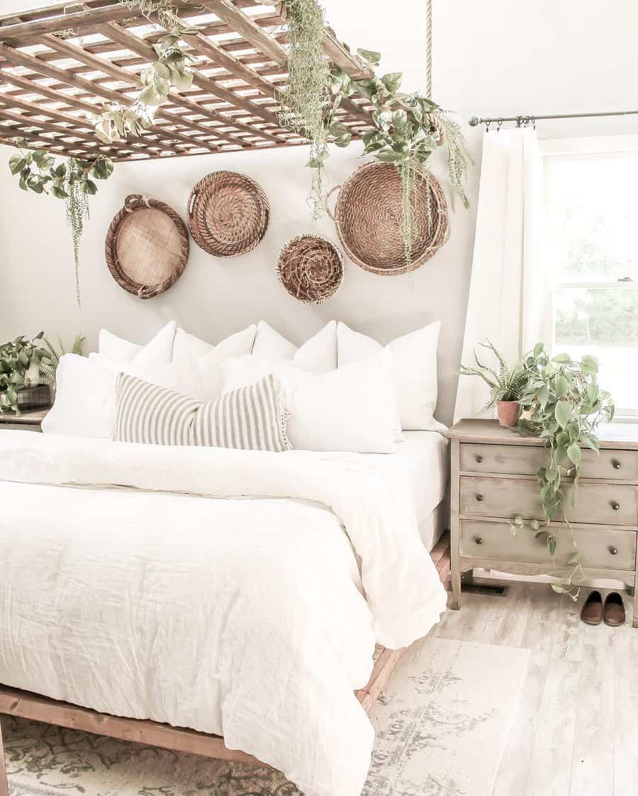 Bright, airy bedroom with white bedding, woven wall baskets, green plants, and a ceiling trellis with hanging greenery