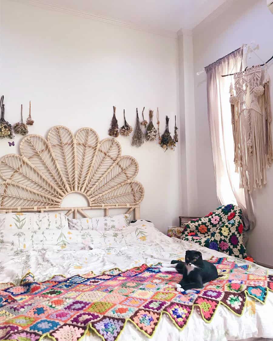 Bohemian bedroom with a wicker headboard, floral bedding, crochet blankets, wall hangings, and a black cat on the bed