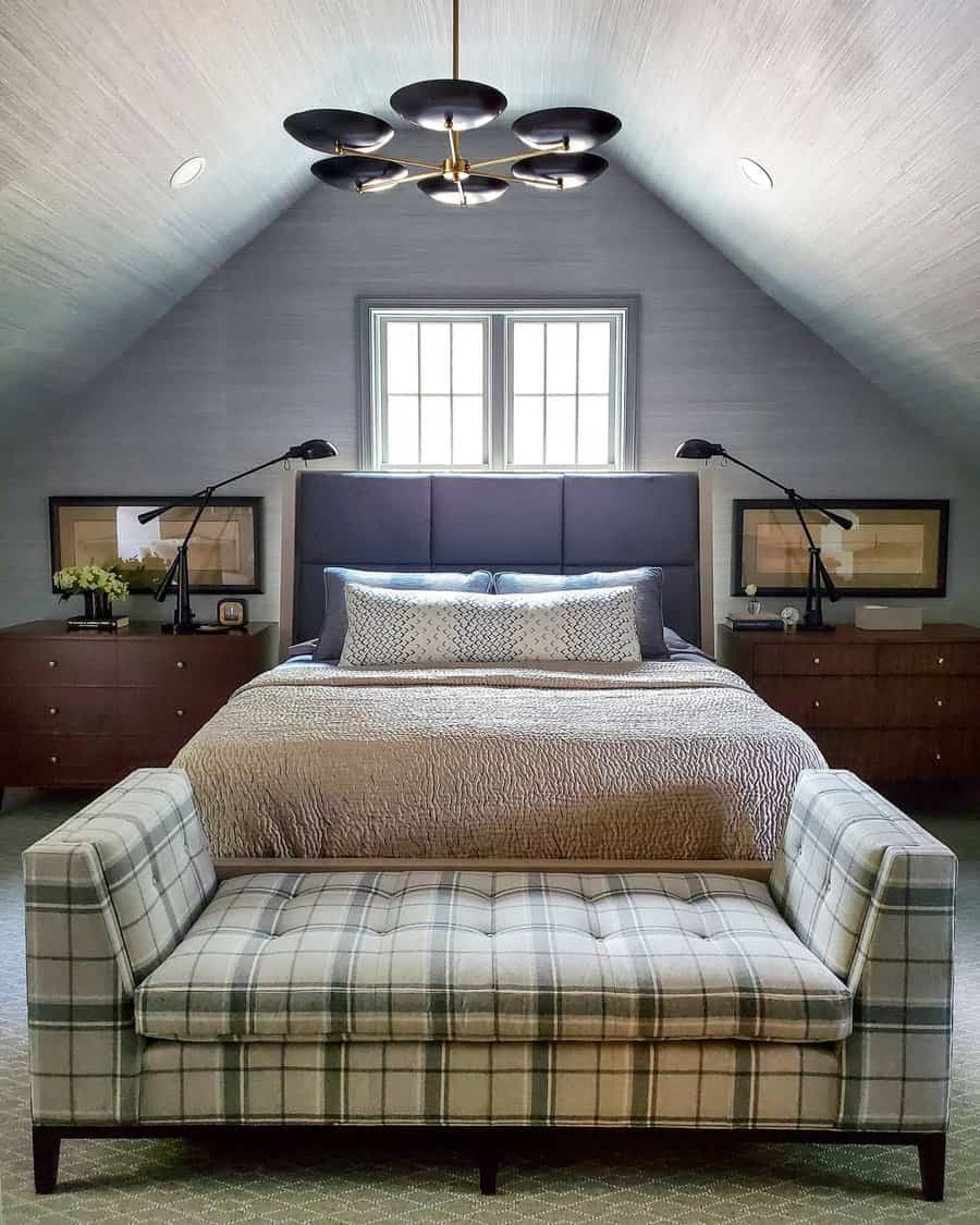 Sophisticated attic bedroom with a modern chandelier, plush bedding, and a plaid loveseat. Dark wood accents create a cozy yet refined space.