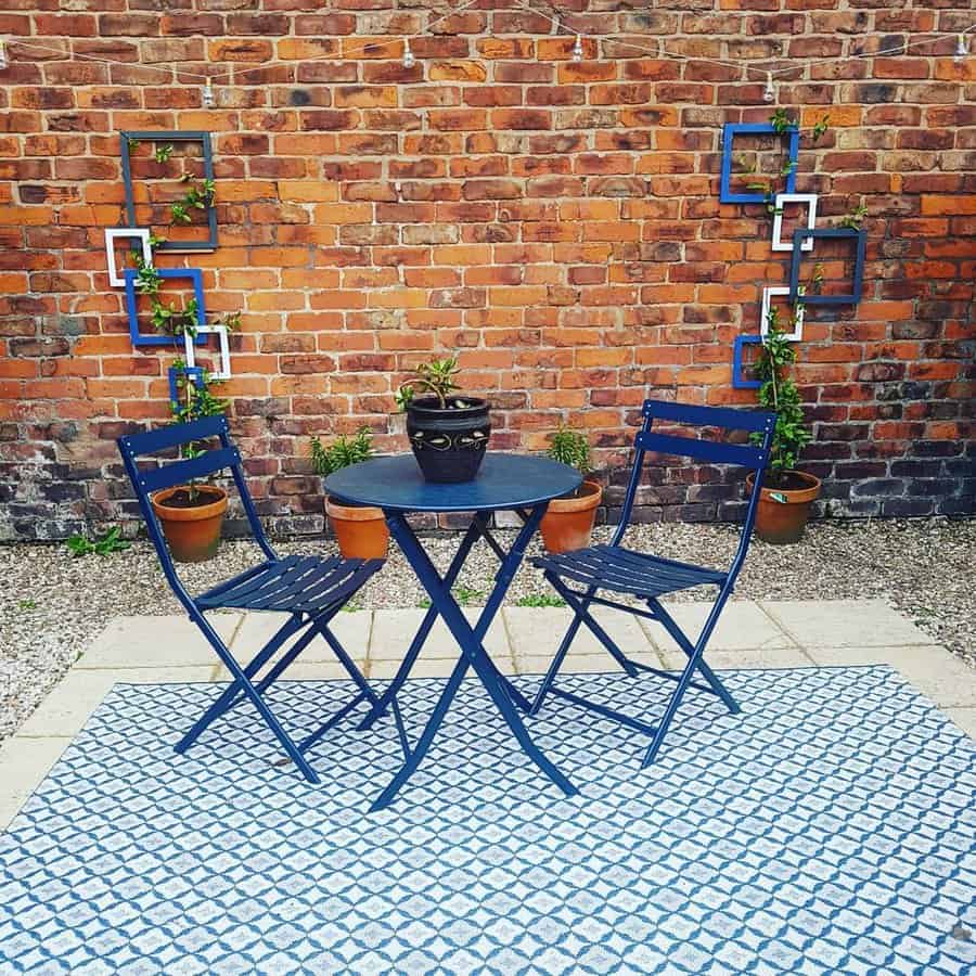 Charming patio with a brick wall, geometric plant trellises, blue bistro set, potted greenery, and a patterned outdoor rug