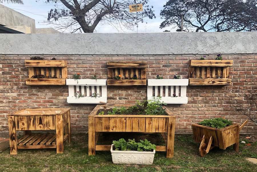 Wooden planters and shelves with green plants against a brick wall outdoors