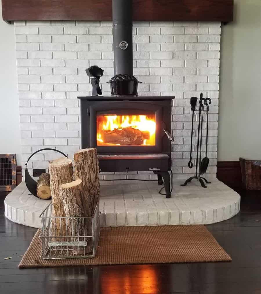 Rustic wood stove with a white brick hearth, firewood storage, and black fireplace tools, creating a cozy and inviting ambiance.