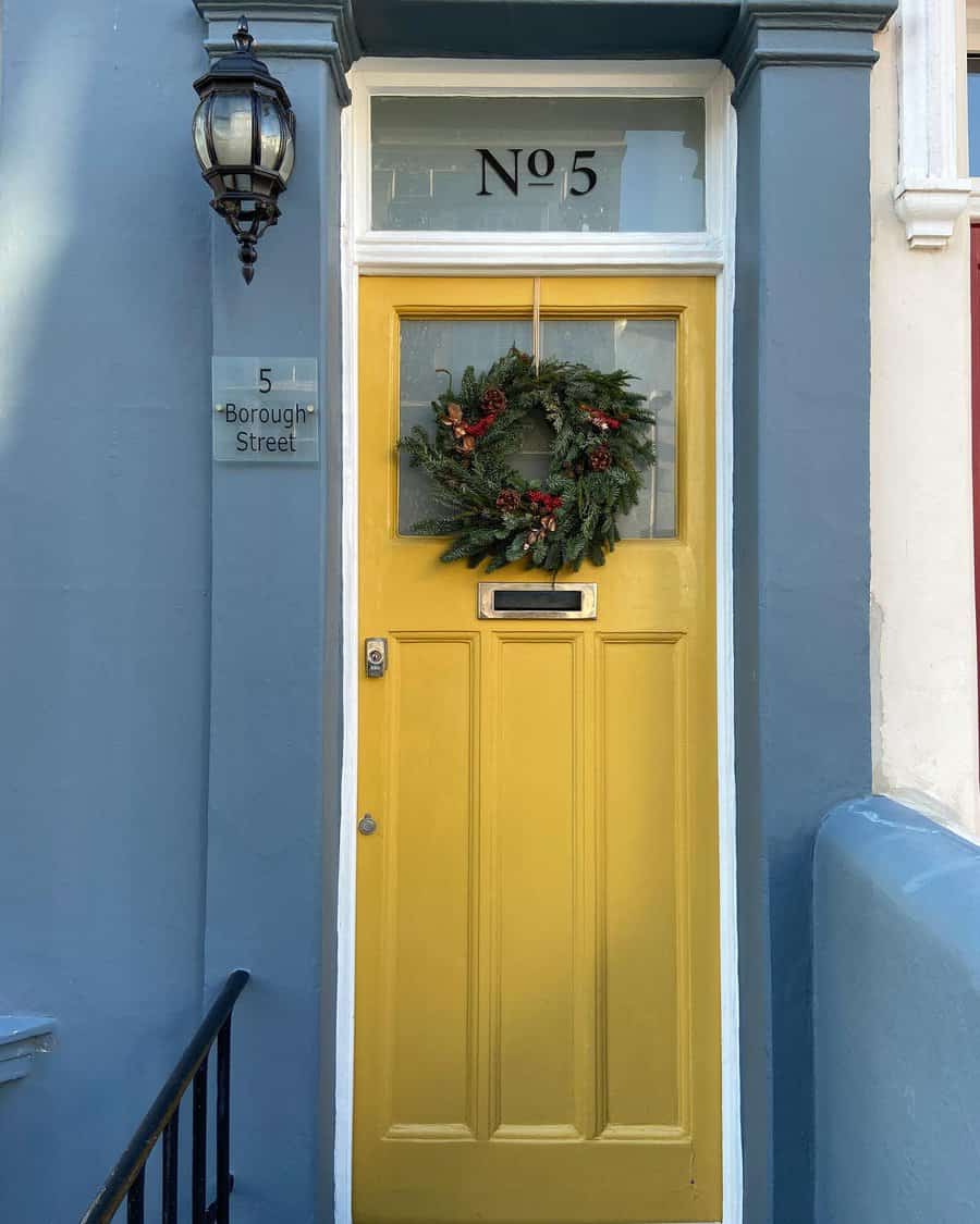 Yellow door with a green wreath, marked "No 5," next to a sign reading "5 Borough Street" with a blue wall and decorative lamp above