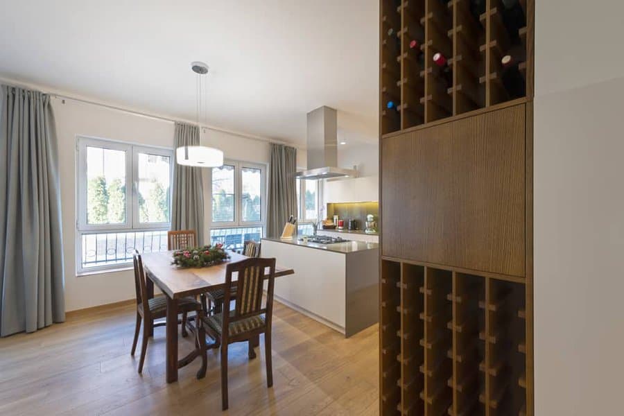 Modern open-plan kitchen with a built-in wooden wine rack, sleek island, and dining area with natural light and warm wood tones