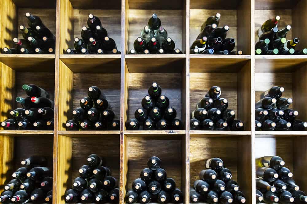 Wooden wine rack with bottles stored horizontally in a grid pattern, forming neat triangular arrangements in each cubby