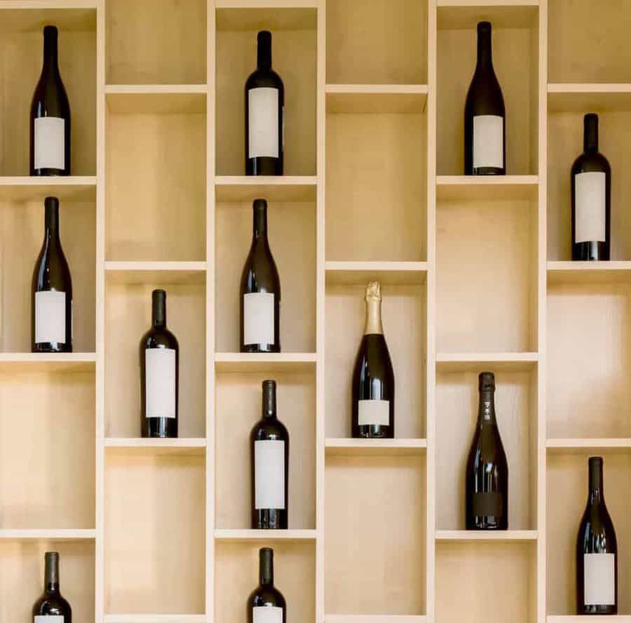 Wooden shelves holding various wine bottles, including some with sparkling wine, arranged in a grid pattern against a light background