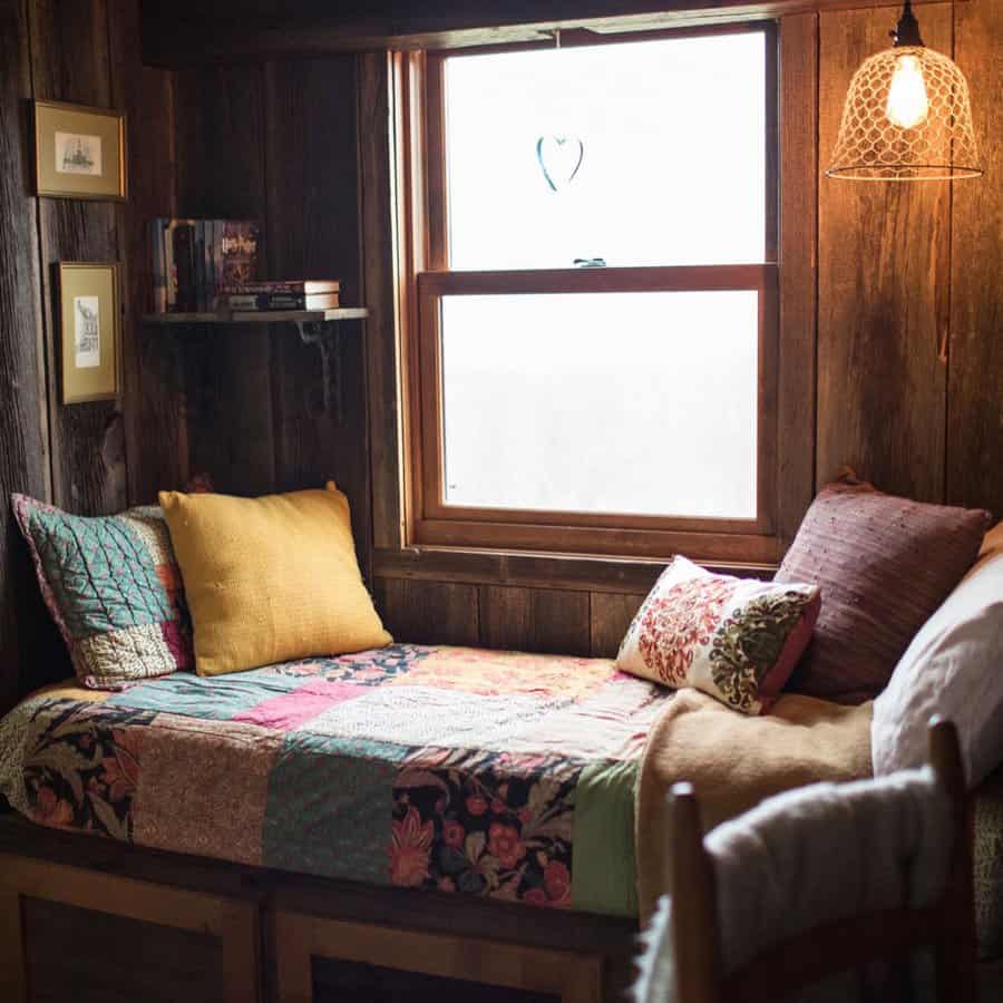 Cozy built-in daybed with a rustic wood backdrop, patchwork quilt, and warm-toned pillows, creating a snug reading nook by the window