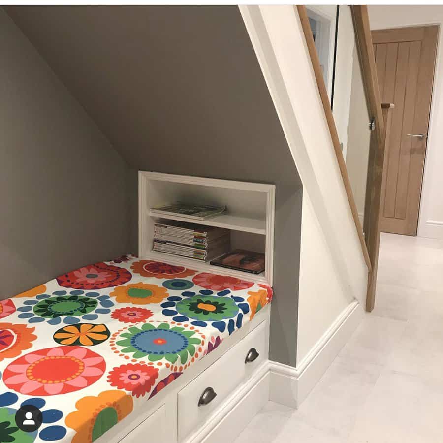 Under-stair built-in daybed with storage drawers, a bold floral cushion, and a small bookshelf, creating a cozy and functional nook