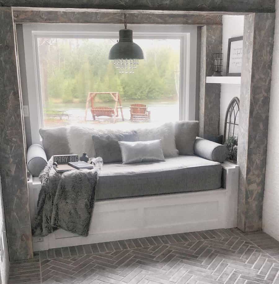 Cozy built-in daybed framed by rustic beams, soft gray cushions, and a faux fur throw, offering a perfect window seat with a serene view