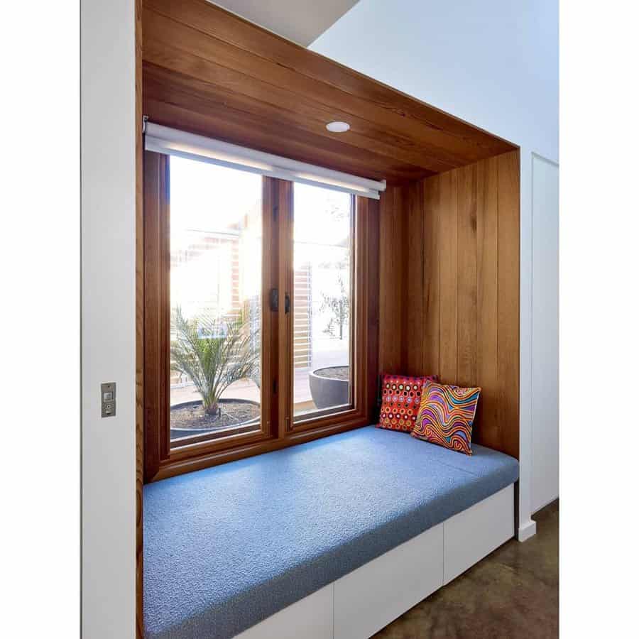 Modern built-in daybed with a blue cushion, wood-paneled nook, and storage drawers, creating a cozy window seat with a view of the garden