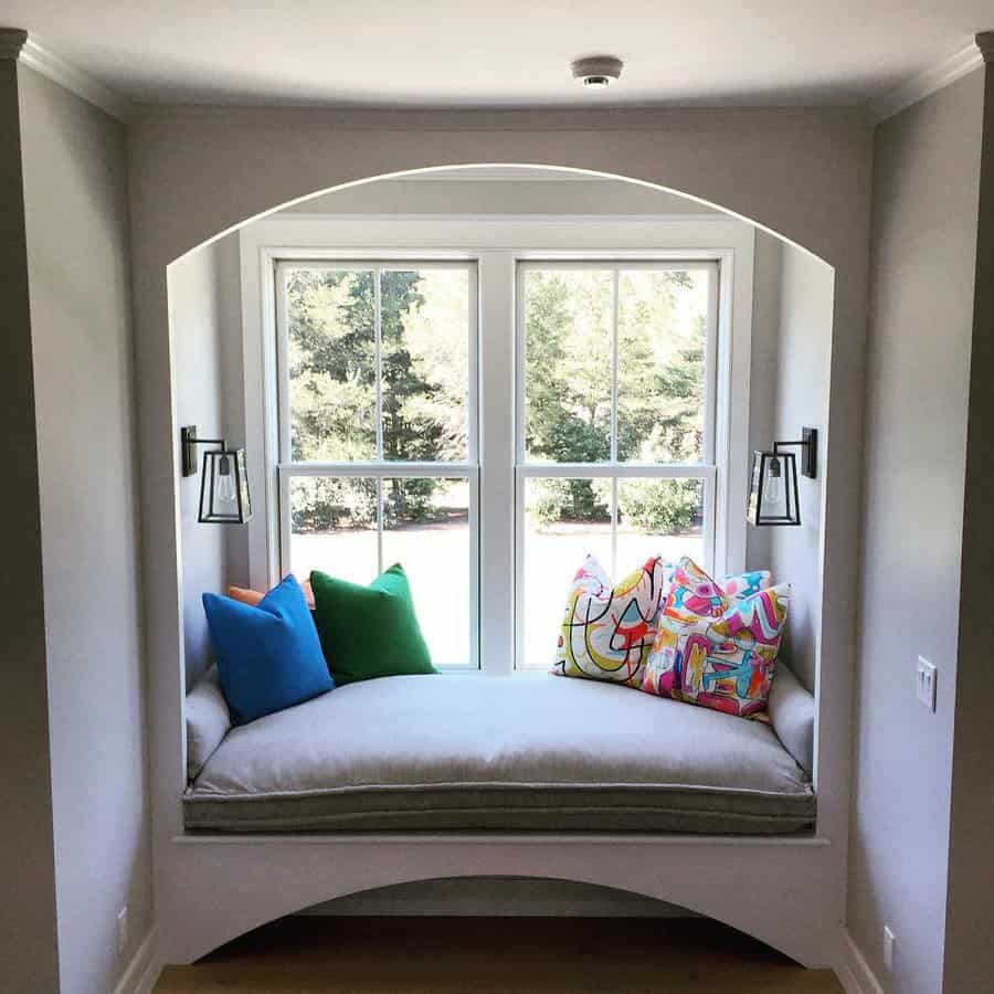 Elegant built-in daybed with plush cushions, colorful throw pillows, and arched detailing, creating a cozy window nook with a scenic view