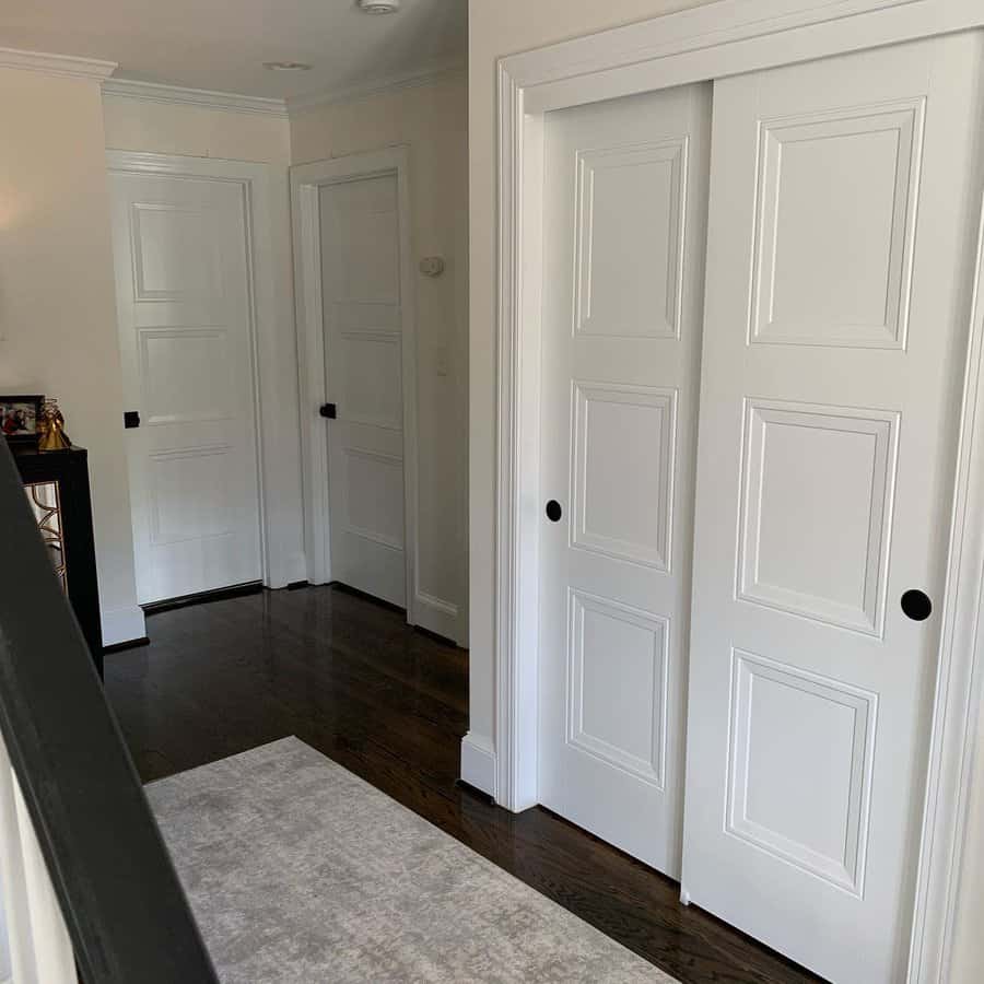 Classic white paneled bypass closet doors with black recessed handles complement the elegant hallway with dark wood flooring and neutral decor