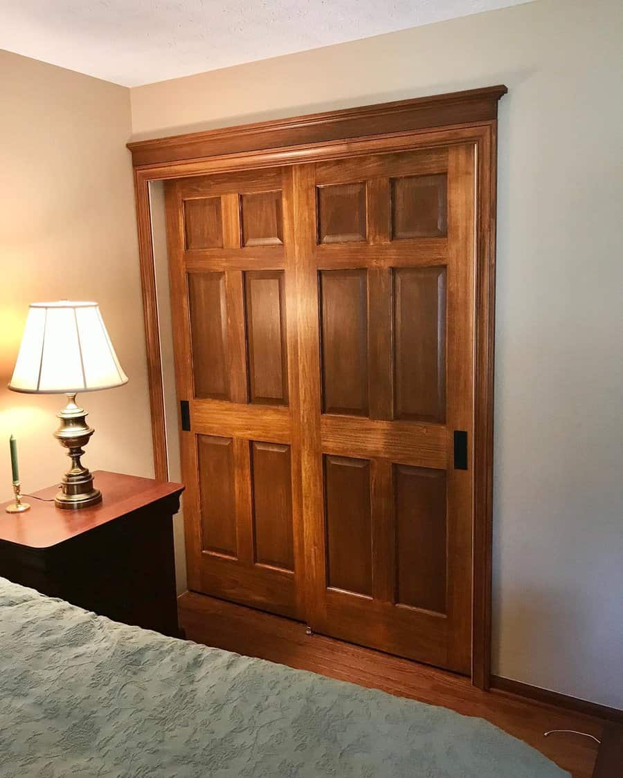 Wooden sliding closet doors in a room with a bedside table and a lamp